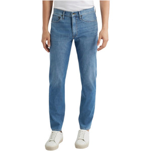 A person wearing Rag & Bone Fit 2 Airflex jeans in light blue, paired with a white t-shirt and white sneakers, stands against a plain background.