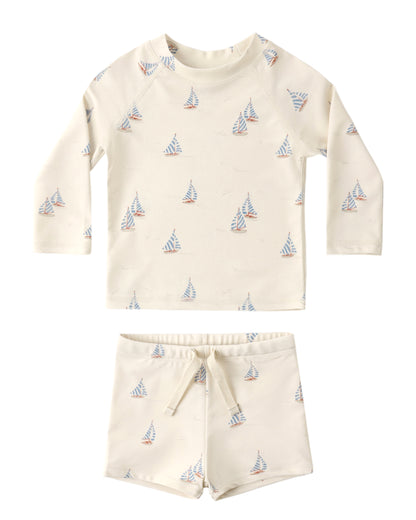 The Rylee & Cru Baby Boys' Rashguard Set features long sleeves in off-white with blue and orange sailboat prints. This UPF 50+ swimwear offers stylish sun protection for all your child’s water adventures.