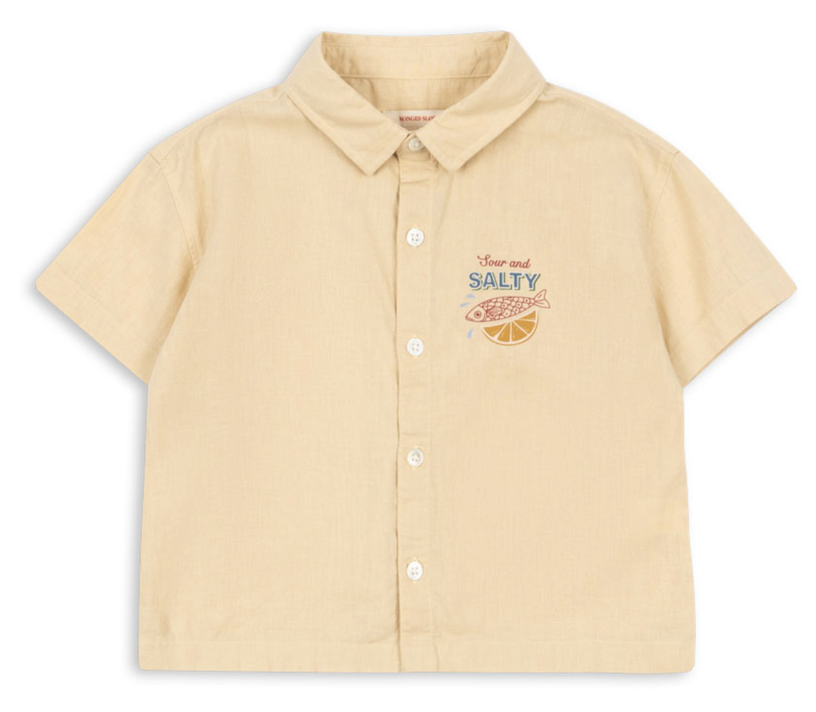 Introducing the Konges Slojd Baby Boys’ and Boys’ Franzen Short Sleeve Linen Shirt—a breathable button-up crafted from a beige linen blend. This collared shirt features short sleeves and is detailed with an embroidered fish, a lemon slice, and the words “Sour and SALTY” on the left chest, making it perfect for effortless style and comfort.