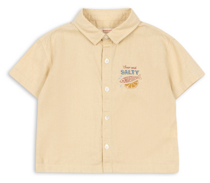 Introducing the Konges Slojd Baby Boys’ and Boys’ Franzen Short Sleeve Linen Shirt—a breathable button-up crafted from a beige linen blend. This collared shirt features short sleeves and is detailed with an embroidered fish, a lemon slice, and the words “Sour and SALTY” on the left chest, making it perfect for effortless style and comfort.