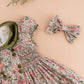 The Kidiwi Girls' Rison Smocked Dress features an olive velvet collar, a matching fabric bow, and pink floral details on a peach background.