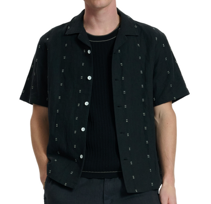Wearing the Rag & Bone Avery Embroidered Camp Shirt in black over a ribbed shirt and dark pants, a person stands against a plain background.