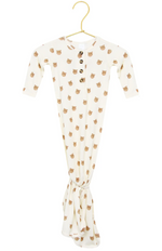 The Lou Lou & Company Baby Teddy Knotted Gown, featuring a cream color, long sleeves, wooden buttons, and an adorable bear face print, hangs on a gold hanger. This tie-bottom gown is designed with a knotted bottom for easy diaper changes and includes a convenient button-down front.