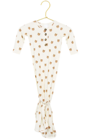 The Lou Lou & Company Baby Teddy Knotted Gown, featuring a cream color, long sleeves, wooden buttons, and an adorable bear face print, hangs on a gold hanger. This tie-bottom gown is designed with a knotted bottom for easy diaper changes and includes a convenient button-down front.