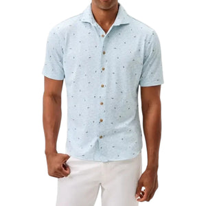A man wearing a Johnnie-O Rowing Shirt in light blue with short sleeves and a subtle print pattern, paired with white pants, standing against a plain white background.