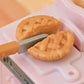 A close-up of a lattice-topped pie being sliced in half with a knife on a pink surface—perfect for imaginative play or as an interactive accessory in the Calico Critters Playful Starter Furniture Set.