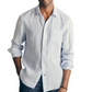A man stands indoors next to a surfboard wearing the Faherty Laguna Linen Shirt, a lightweight light blue and white striped button-up with rolled sleeves.