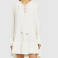 A woman models the Lanvin Flared Pleated Dress with Long Sleeves, a loose-fitting white mini dress featuring a lace-up neckline, ruffled hem, and delicate pleats, set against a plain light background.