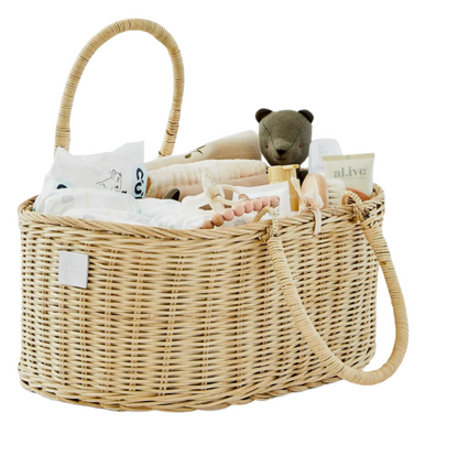 The BSavannah Diaper Caddy by Bebe Bask is an eco-friendly rattan wicker bassinet containing essentials like a teddy bear, folded clothes, and bottles. Its removable foam divider ensures organization and easy access.