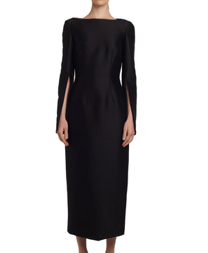A person wears the Adam Lippes Talitha Silk Wool Twill Dress, a long black Japanese silk wool design with a high boat-neck and split sleeves, standing against a white background.