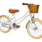 The Banwood Classic Children’s Bicycle features a white frame, tan tires, brown leather seat and handlebars, plus a cute wicker basket—ideal for stylish young riders.