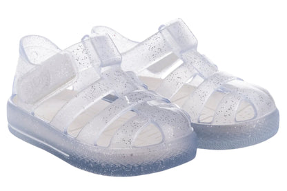 The Igor Girls' Star Jelly Sandal features translucent PVC with silver glitter, closed toes, adjustable ankle straps, textured soles, and classic water sandal comfort.