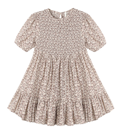The Girls’ India Dress by Rylee & Cru features short sleeves, a knee-length silhouette, a light brown floral pattern, a smocked bodice, gathered waist, and a ruffled hem.
