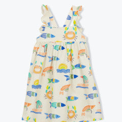 The Girls' Fredine Dress by Arsene & Les Pipelettes is a sleeveless cream apron dress with ruffled straps, decorated with a vibrant ocean print featuring colorful fish, crab, and sun motifs.
