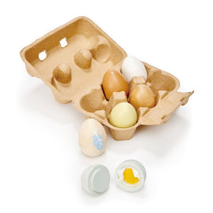 A Tender Leaf Toys Wooden Eggs set featuring a cardboard egg carton containing five wooden eggs, including one painted white, with two halves of a toy egg displaying a yellow yolk placed in front of the carton.
