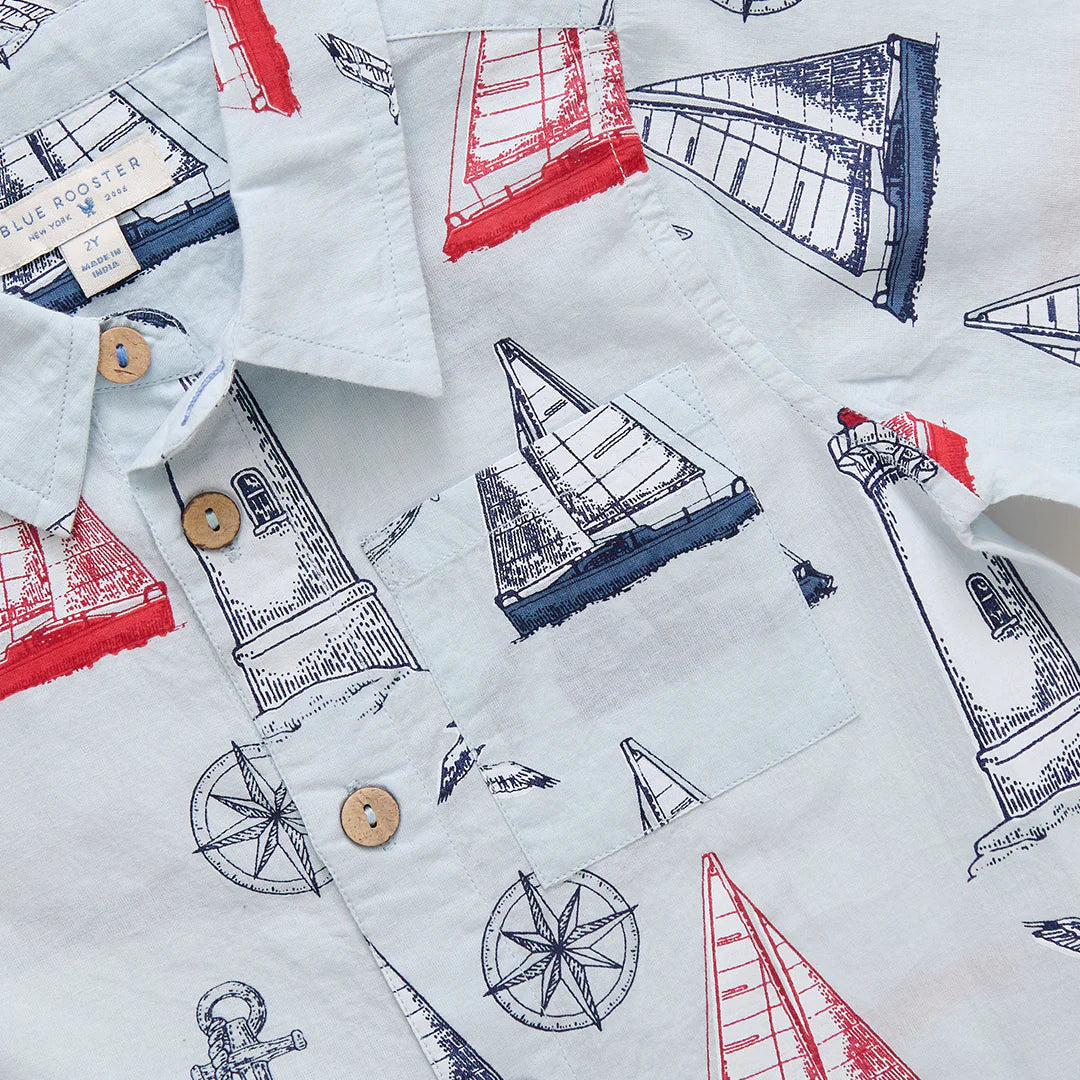 The Baby Boys' Easton Jumper by Pink Chicken is a light blue collared short sleeve button-up with red and navy sailboats, lighthouses, anchors, and compasses—ideal for little ones’ nautical adventures.