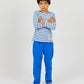A young boy with short brown hair stands barefoot, arms crossed, wearing the Arsene & Les Pipelettes Boys' and Girls' Sailor Shirt—a nautical-inspired blue and white Breton striped top—paired with bright blue pants in soft organic cotton jersey against a plain light background.