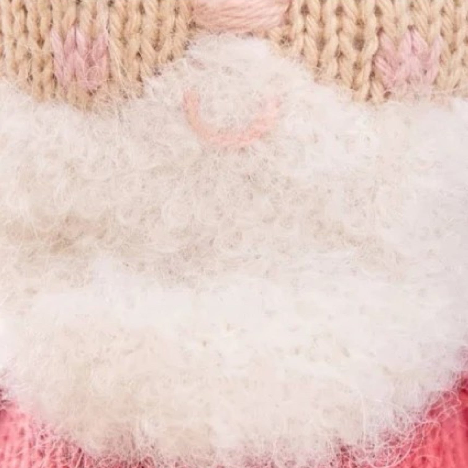 Close-up of Cuddle + Kind’s Baby Santa, a soft baby toy handcrafted from cotton yarn, featuring a beige and pink face, white fluffy beard, and faint pink smile that highlights the texture and stitching details.