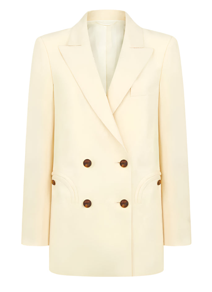 The Savannah Everyday Blazer by Blaze Milano is a classic cream-colored piece featuring a double-breasted design with brown buttons, peak lapels, two front pockets, and crafted from a luxurious silk and linen blend.