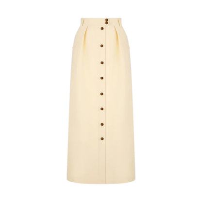 The Savannah Nija Skirt by Blaze Milano is a high-waisted, full-length cream skirt with elegant front pleats and a row of dark buttons down the center.