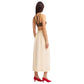 A woman faces away in a brown strappy top, Blaze Milano's Savannah Nija Skirt—a high-rise beige linen silk midi skirt—and red heels, set against a white background.