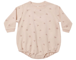 The Quincy Mae Baby Girls’ Crewneck Bubble Romper is a long-sleeved, light pink organic cotton outfit featuring small heart patterns and convenient snap buttons at the bottom for easy diaper changes.