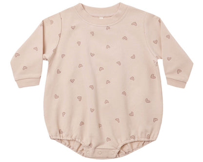 The Quincy Mae Baby Girls’ Crewneck Bubble Romper is a long-sleeved, light pink organic cotton outfit featuring small heart patterns and convenient snap buttons at the bottom for easy diaper changes.