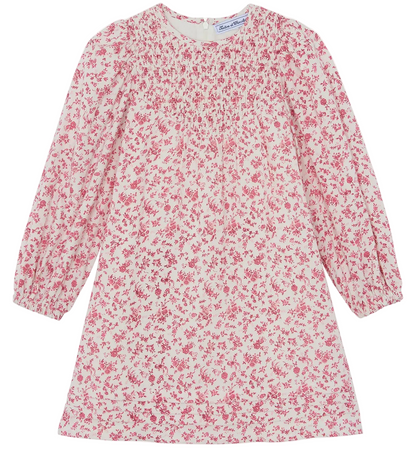 The Girls’ Flowery Print Cotton Dress by Tartine et Chocolat is a long-sleeved dress for girls, made from unbleached cotton with a white base, decorated with a pink floral print and gathered detailing at the chest, shown laid flat against a white background.