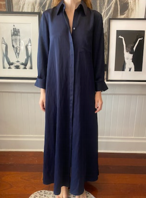 A person stands barefoot on a patterned rug wearing TWP's dark blue Jenny's Coated Linen Gown. In the background, two framed black and white photos adorn the wall.
