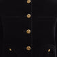 A close-up of the Jealousy Shamo Bolero by Blaze Milano, a black cotton velvet jacket with gold-toned buttons and four front pockets, worn by a person.