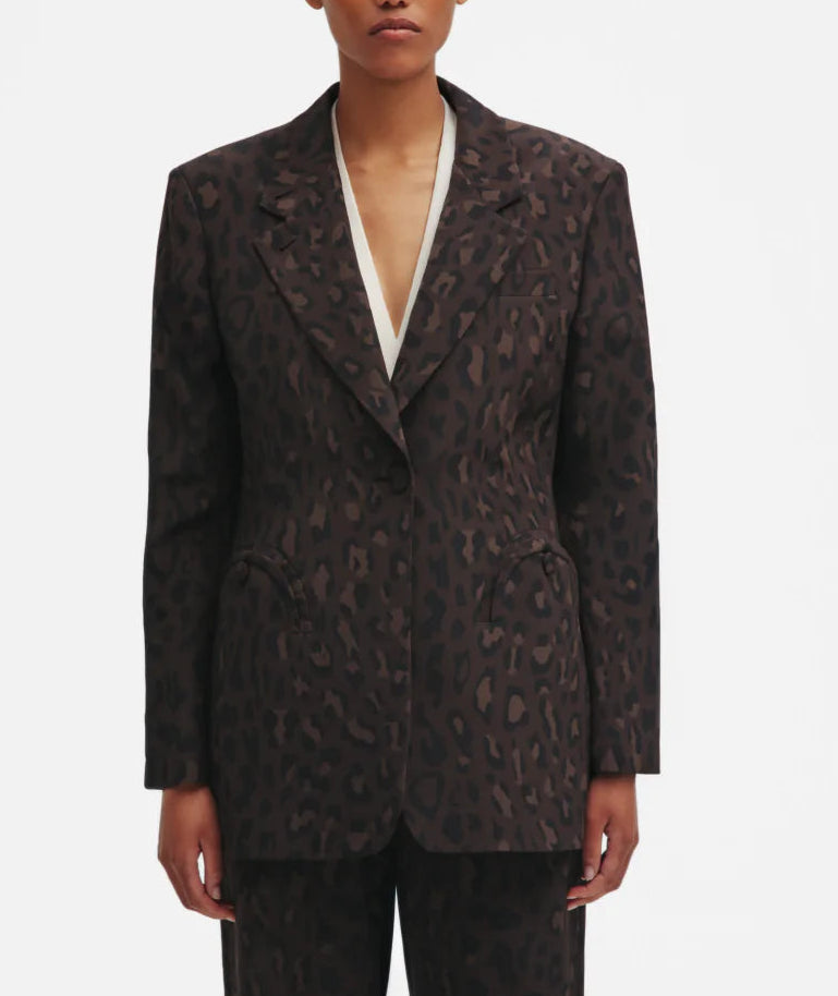 A person wears the Blaze Milano Simba Daisy Blazer in dark brown leopard print with structured shoulders and matching pants, standing against a plain white background.