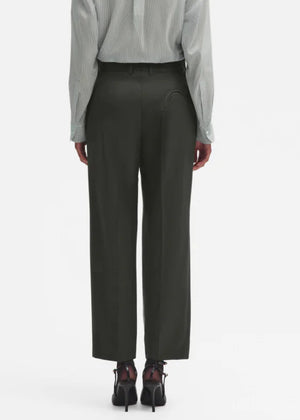 A person wearing a light gray long-sleeve shirt, Blaze Milano Nahalin Fox Pants in green, and black heeled shoes is shown from the back against a plain white background.