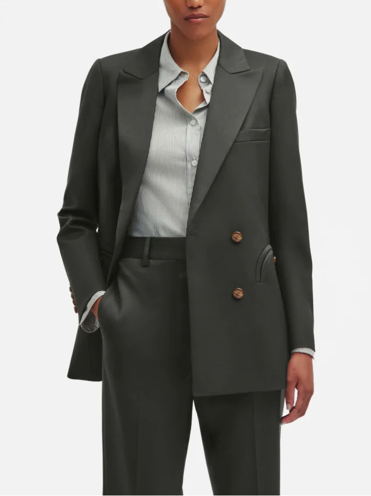 Someone wearing the Nahalin Everyday Blazer by Blaze Milano—a dark, double-breasted wool mohair piece—paired with a light striped button-up shirt, photographed from shoulders to mid-thigh.