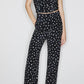 A woman models the Mariquita Nana Pants by Blaze Milano—high-waisted, straight-leg black pants with white polka dots—paired with a black one-shoulder sleeveless top and black high heels.