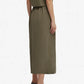 A person stands facing away, wearing the Blaze Milano Midday Sun Nija Skirt in palm green and gray shoes, with arms relaxed by their sides against a plain white background.