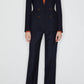 A person wears the Blaze Milano First Class Charmer Blazer over an orange collared shirt with open-toe heels, standing against a plain white background.
