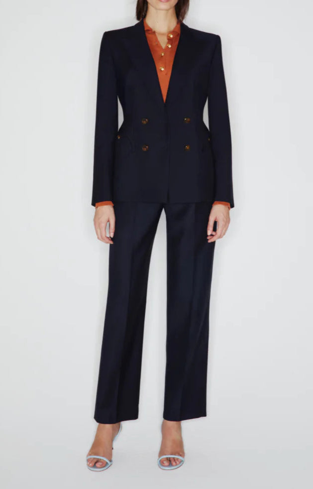 A person wears the Blaze Milano First Class Charmer Blazer over an orange collared shirt with open-toe heels, standing against a plain white background.