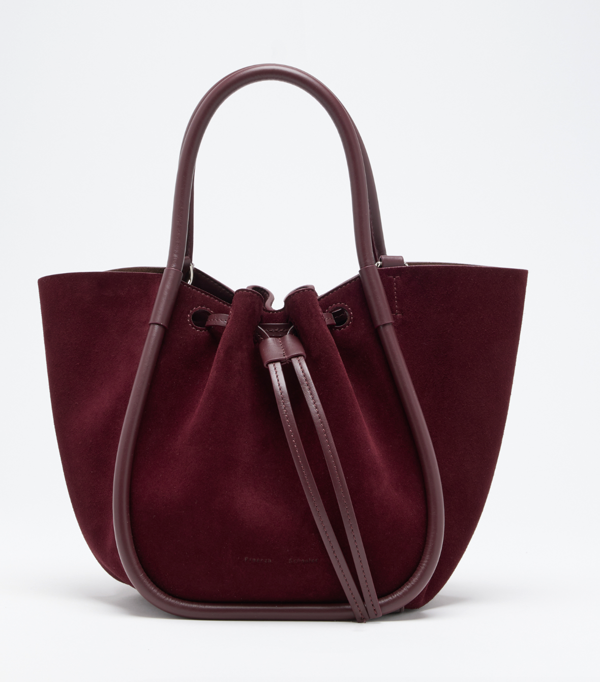 The Proenza Schouler Small Ruched Soft Suede Tote, in burgundy with leather handles and a drawstring closure, displays a sculptural silhouette against a plain white background.