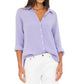 A woman wears the Xirena Scout Shirt with rolled sleeves and white pants, standing against a plain white background.