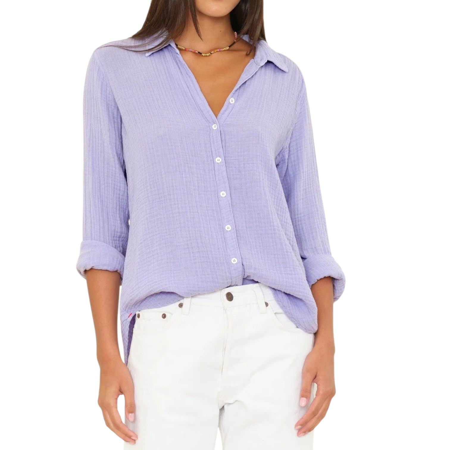 A woman wears the Xirena Scout Shirt with rolled sleeves and white pants, standing against a plain white background.