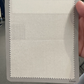 A hand holds a rectangular card showing a white fabric swatch with pinked edges—ideal inspiration for Samuelsohn Slim Fit Flat Front Wool Pants—set against a neutral background.