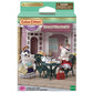 Two rabbit figurines are seated at a garden table with tea and treats outside a pink building. The packaging displays the name “Tea and Treats Set” from Calico Critters and contains delightful tea party accessories to complete the charming scene.
