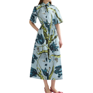 A person wearing the Erdem Etched Tulip Short Sleeve Shirt Dress, featuring a light blue cotton poplin with a bold botanical print, paired with pink shoes, stands against a white background.