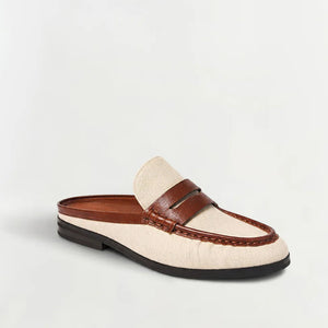 The Dean Canvas Como Loafer Mule from Simkhai features a cream-colored canvas upper with brown leather strap and trim, a black sole, and stitched detailing. This stylish backless loafer is displayed on a plain white background.