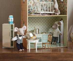 A dollhouse kitchen scene features two Maileg toy mice as chef and waiter, with miniature furniture including a fridge, crib, and the Maileg Side Table, Mouse—plus a mouse castle complete with a cheesy snack.