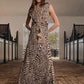 A woman stands in a stable hallway wearing the ankle-length Silent Rising Dress by Johanna Ortiz, crafted from double-sided jersey and adorned with an elegant black and white External Feathers motif, complemented by a long necklace.