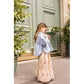 A young girl wearing the Louis Louise Girls’ Rachel Skirt and a denim jacket stands on a sidewalk in front of a large green door, looking down at something in her hands.