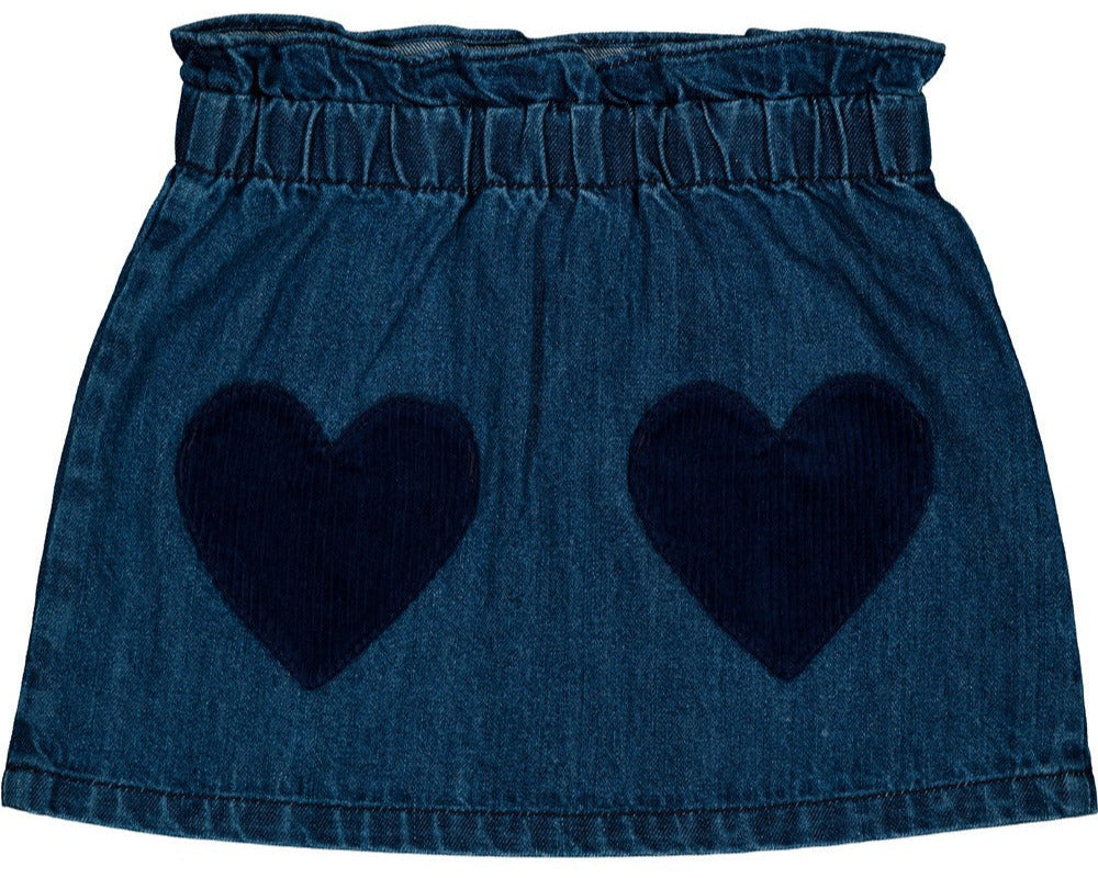 The Louis Louise Girls' Teacher Washed Denim Skirt is a blue denim mini skirt featuring an elastic waistband and two large, dark blue heart-shaped front pockets.
