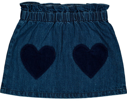 The Louis Louise Girls' Teacher Washed Denim Skirt is a blue denim mini skirt featuring an elastic waistband and two large, dark blue heart-shaped front pockets.