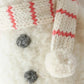 Close-up of the “Baby Snowman - Candy Cane” by Cuddle + Kind, a handcrafted figure made from cotton yarn, featuring a fluffy white body, two black buttons, and a scarf with red stripes.